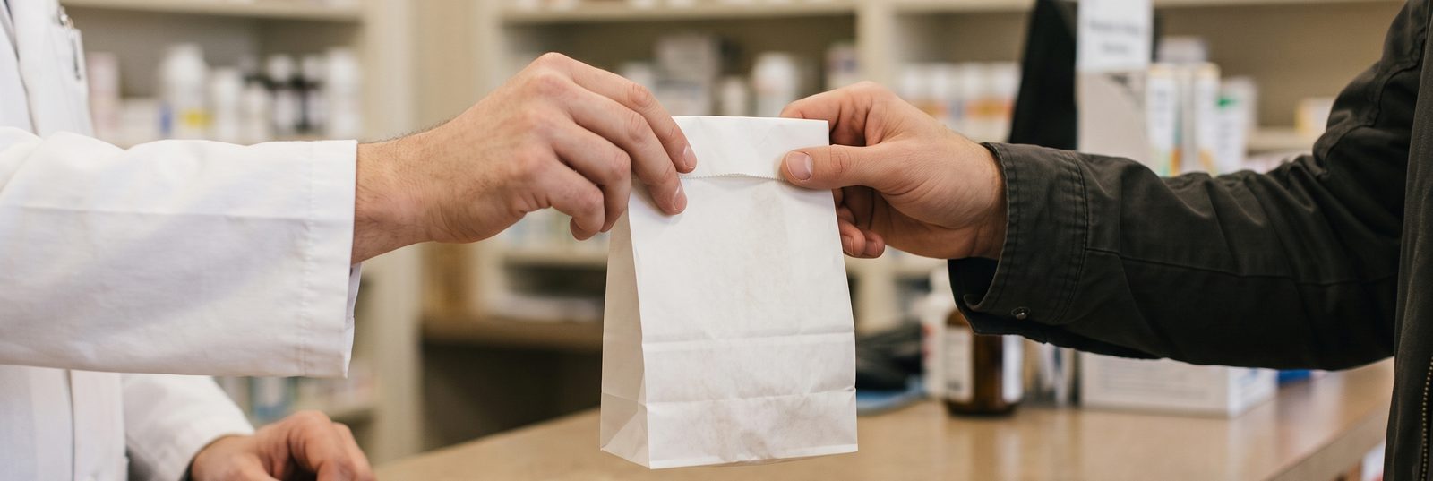 A pharmacist handing a prescription bag across a local pharmacy counter