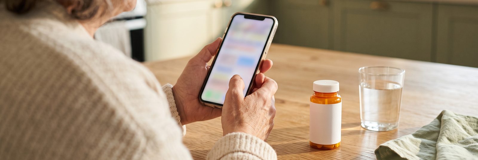 A member checking her phone at the kitchen table, a prescription bottle and a glass of water beside her